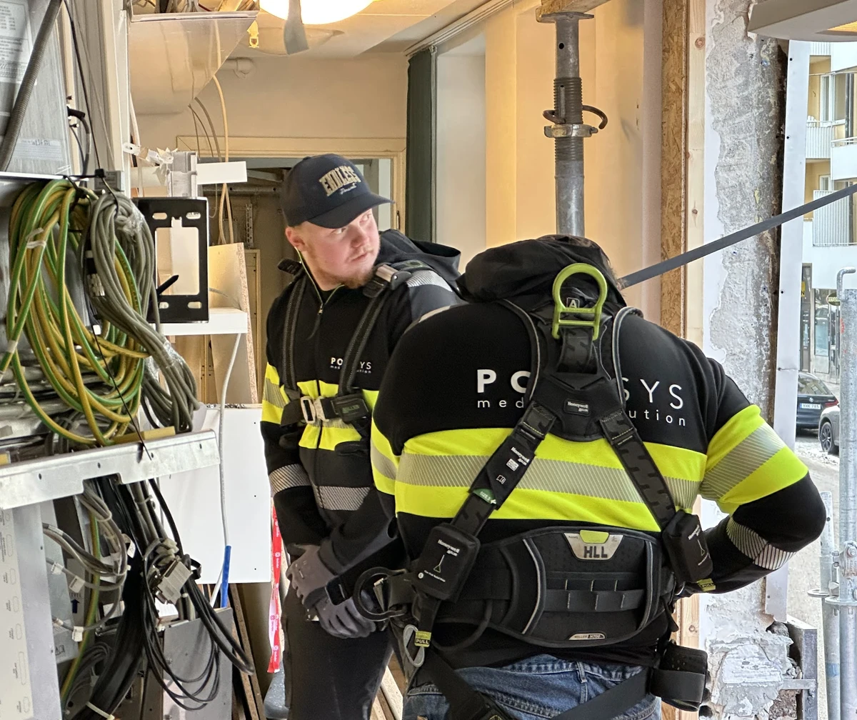 Två Polysys-tekniker i varselkläder hanterar medicinteknisk utrustning på en sjukhusbyggarbetsplats