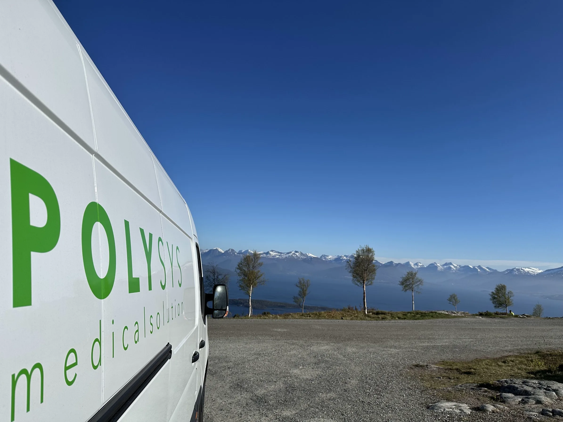 Polysys-bil framför fjord och snöklädda fjäll